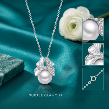 Silver pendant necklace with a large white pearl and a butterfly-shaped crystal setting, displayed on teal satin fabric with a white flower and three detail inset images. The text 'SUBTLE GLAMOUR' appears below.